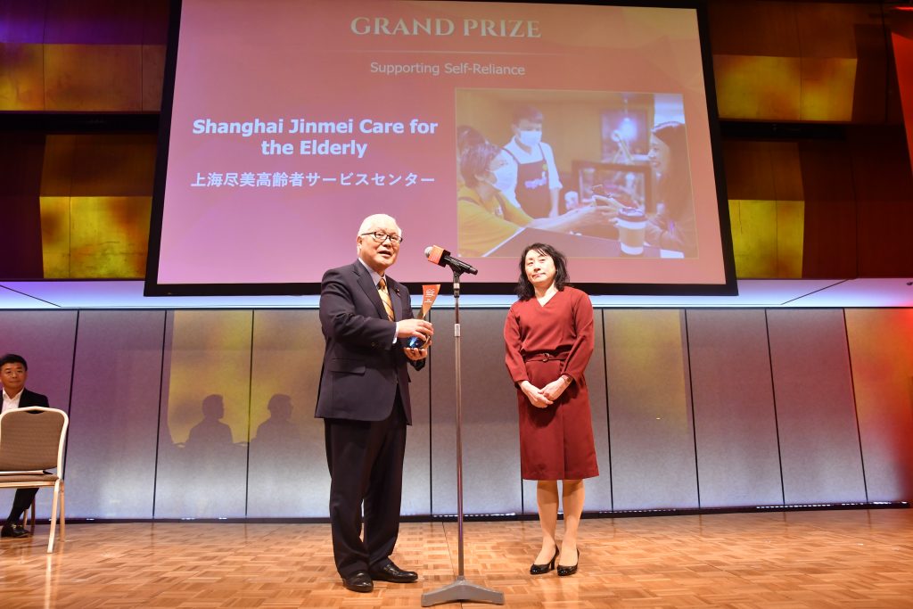 On behalf of Jinmei Care of Shanghai, Ms. Wang Qing accepts the Grand Prize for Supporting Self-Reliance. Ms. Gu Chunling, founder of Jinmei Care, sent a video message.